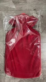 Image file description: A red heating bag hanging inside a transparent plastic bag on a wooden floor.